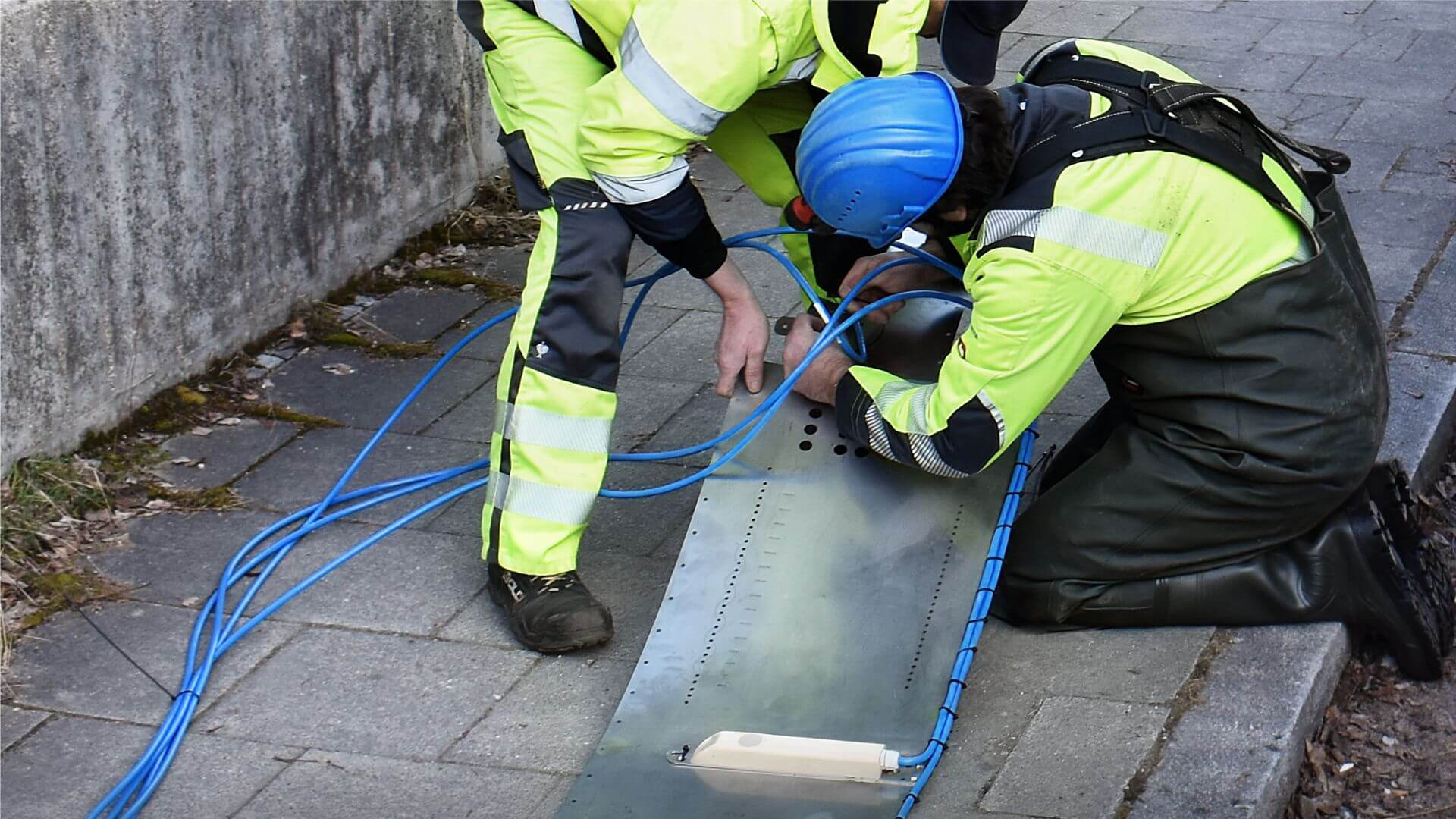 Zwei NIVUS-Techniker montieren einen Sensor an das Rohrmontagesystem auf einem gepflasterten Bordstein.
